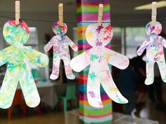 paper cut out people hanging from clothes pins on a line in front of colorful striped poles