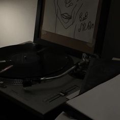 a record player sitting on top of a table next to a framed drawing and papers