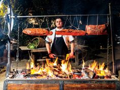 a man standing in front of a fire pit with hot dogs on top of it