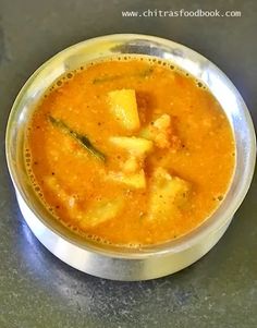 a metal bowl filled with food sitting on top of a gray counter next to a spoon