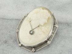 This cameo from the Art Deco era can be worn as a pin or pendant. Delicate looking filigree provides an elegant frame for the sleek bezel setting. This type of cameo is called a “habille”, with a white gold 'necklace' around the neck of the figure, set with a small diamond. Metal: 14K White Gold Gem: Cameo Gem Measurements: 42 x 49 mm, Oval Accents: Diamond .05 Carats Measures: 42 x 49 mm Marks: “14K” Stamped on the reverse Filigree Frame, Art Deco Frame, Art Deco Filigree, Gemstone Brooch, White Gold Necklace, Vintage Jewelry Art, Cameo Jewelry, Gold Brooch, White Gold Necklaces