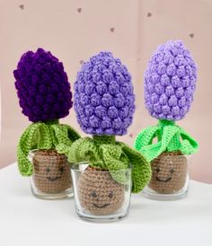 three crocheted flowers in small glass vases with faces drawn on the top