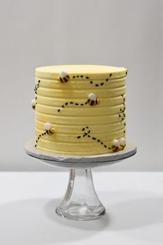 a yellow cake with bees on it sitting on top of a glass stand in front of a white wall