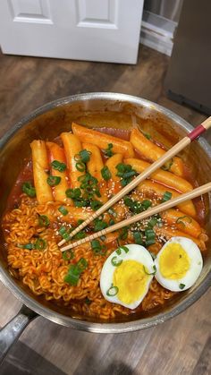 eggs, noodles and carrots are in a pan with chopsticks on the side