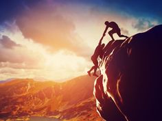 two people climbing up the side of a mountain