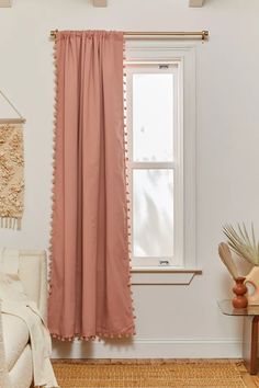 a pink curtain hanging in front of a window with a potted plant next to it