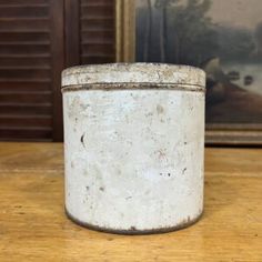 an old white canister sitting on top of a wooden table next to a painting