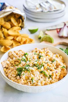 a white bowl filled with rice next to some chips and other food on a table