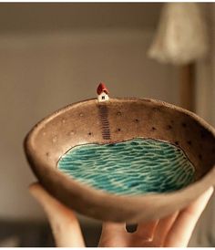 a person holding up a bowl with a small house on it