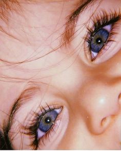 a close up of a child's face with blue eyes and long hair on top of her head