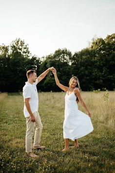 a man and woman holding hands while standing in the middle of a field with trees behind them