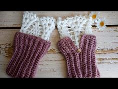 two crocheted mittens sitting on top of a wooden table next to a daisy