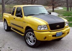 a yellow pick up truck parked in a parking lot next to some grass and trees