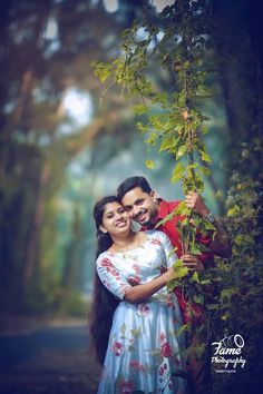 a man and woman standing next to each other in front of green leaves on a tree