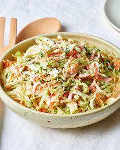 a bowl filled with coleslaw on top of a table next to wooden spoons