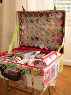 an old suitcase is filled with buttons and other crafting supplies on a wooden table