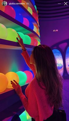 a woman standing next to a wall with colorful lights on it's sides and her hand in the air