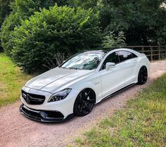 a white mercedes cls parked on the side of a dirt road next to trees