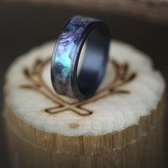 a wedding band with an opalite inlay is on top of a piece of wood