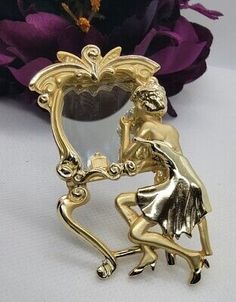 a gold plated figurine holding a mirror in front of a purple flower