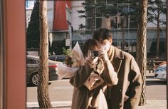 a man and woman are walking down the street with flowers in their hands while taking a selfie