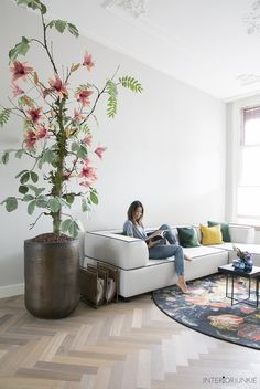 a woman sitting on a white couch in front of a flower pot and a plant