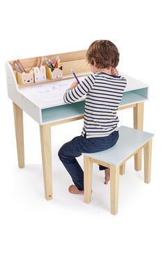 a little boy sitting at a desk with a pencil in his hand and writing on the paper