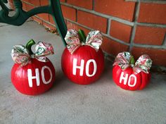 three painted pumpkins with bows on them sitting in front of a brick wall, one has the word ho written on it