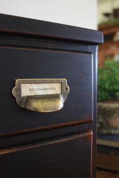 a close up of a drawer with a name plate on it and potted plants in the background