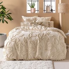 a bed with white comforter and pillows in a room next to a potted plant