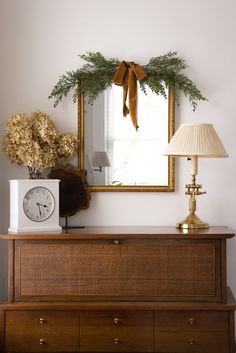 a dresser with a mirror, lamp and clock on it