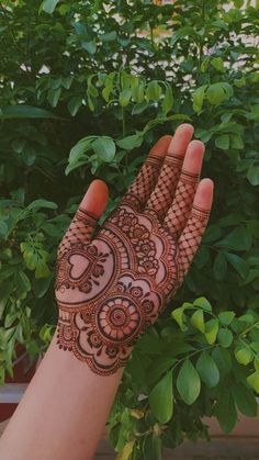 a hand with henna on it and some plants in the back ground next to it