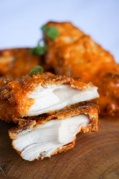 two pieces of chicken sitting on top of a wooden cutting board next to another piece of food