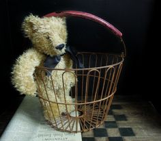 a teddy bear sitting in a wire basket on top of a book with a bow