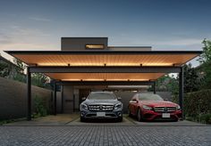 two cars are parked in front of a modern house at night, one is red and the other is black