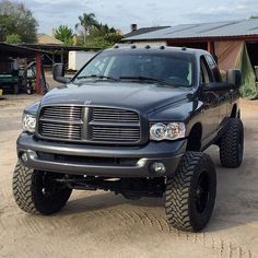 a black dodge ram truck parked in front of a building with large tires on it