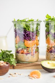 two mason jars filled with salad ingredients on top of a wooden cutting board next to an avocado