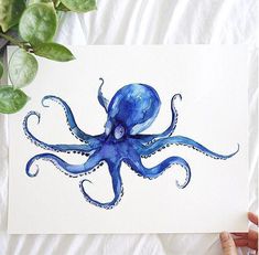 an octopus is painted on a white paper with blue ink and some green leaves next to it