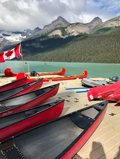 canoes are lined up on the dock with canadian flags flying in the wind and mountains in the background