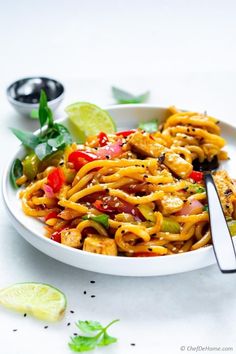 a white bowl filled with noodles and vegetables on top of a table next to lime wedges