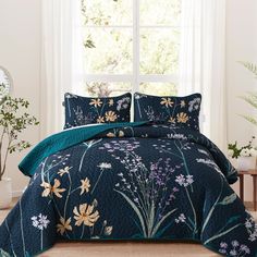 a bed covered in a blue comforter and pillows with flowers on the pillowcase