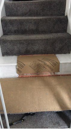 a cardboard box sitting on the bottom of some stairs next to a carpeted stair case