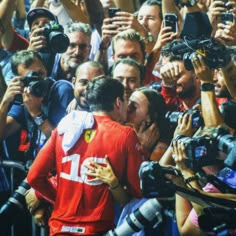 a man is kissing another man in front of a large group of people with cameras