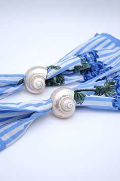 two blue and white scarfs with seashells attached to them on a white surface