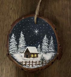 a christmas ornament hanging on a wooden surface with snow and trees in the background