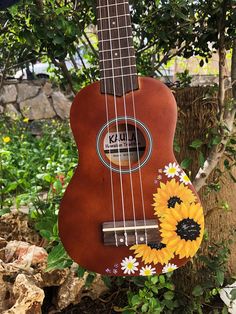 an ukulele with sunflowers and daisies painted on the strings hanging from a tree