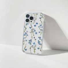 an iphone case with blue flowers on it sitting on a white surface next to a shadow