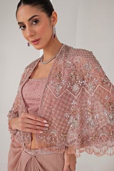 Elevate your style with the stunning Pastel Pink Draped Skirt with Embellished Cape, that effortlessly blends tradition with contemporary elegance. The pink cape features a sophisticated kimono sleeve , adorned with intricate florence embroidery using sequins, crystal tassels, cutdana, and bead highlights, adding a touch of opulence. Paired perfectly with a sequin jaal embellished blouse, it offers a dazzling appeal, making you the center of attention. Completed with a draped skirt, designed for Embroidered Cape, Pink Cape, Pink Kimono, Indian Wedding Wear, Embellished Blouse, Draped Skirt, Kimono Sleeves, Kimono Sleeve, Wedding Wear