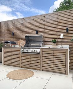 an outdoor kitchen with grill, sink and table in front of a wooden privacy wall