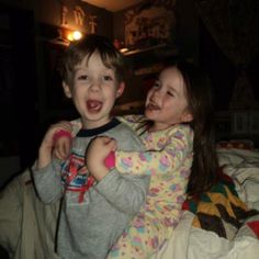 two young children playing on a bed in the dark with their arms around each other